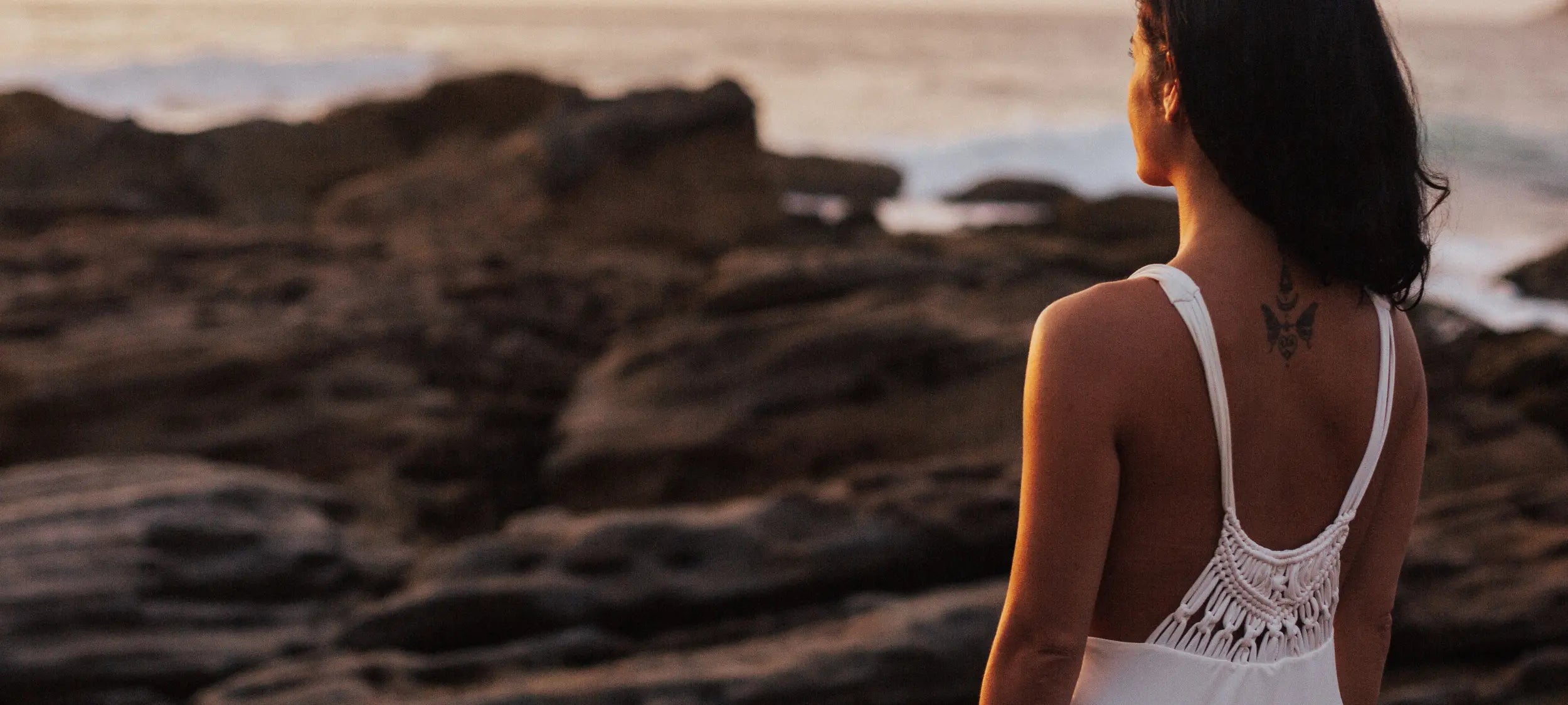 Woman in a white dress standing on rocky beach at sunset