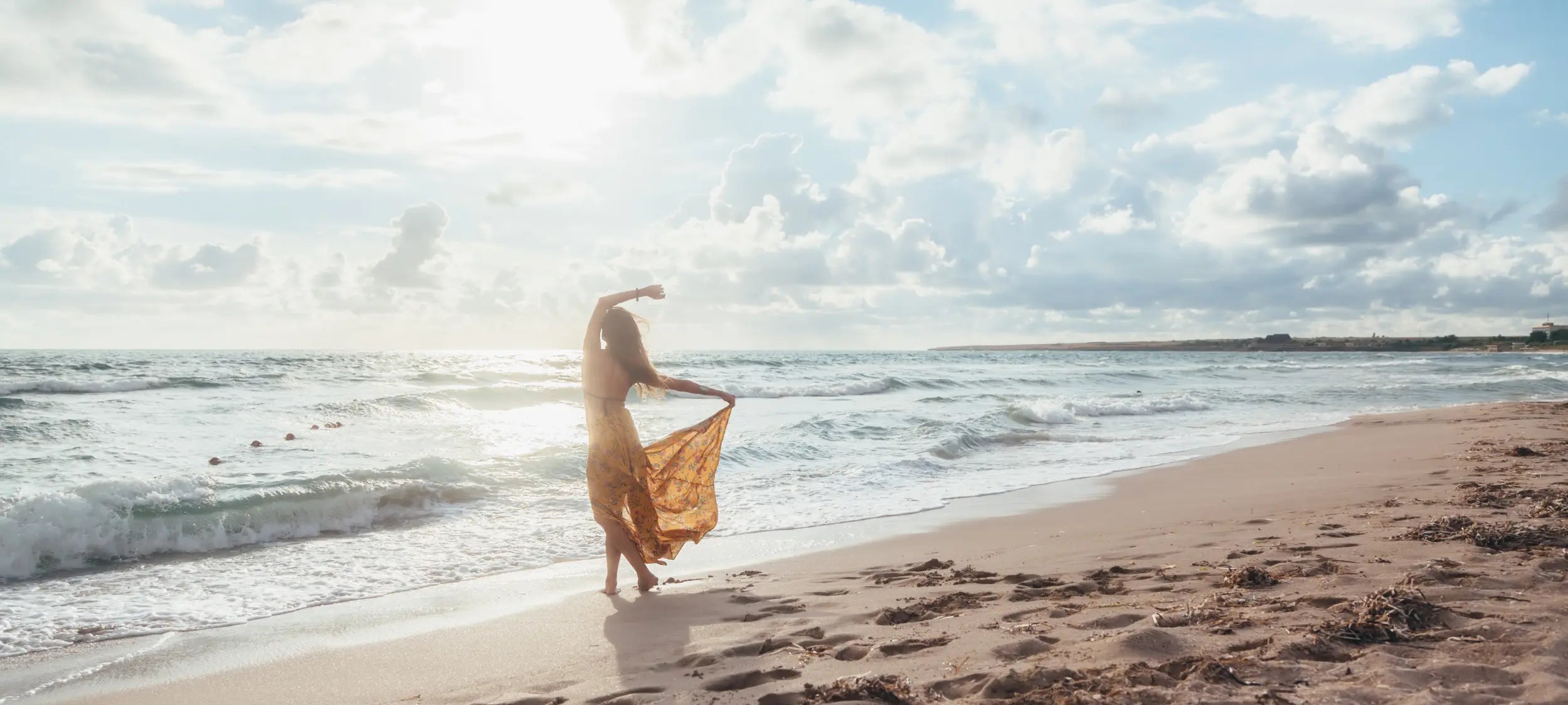 Woman in a yellow dress standing on a beach with waves and sky in the background
