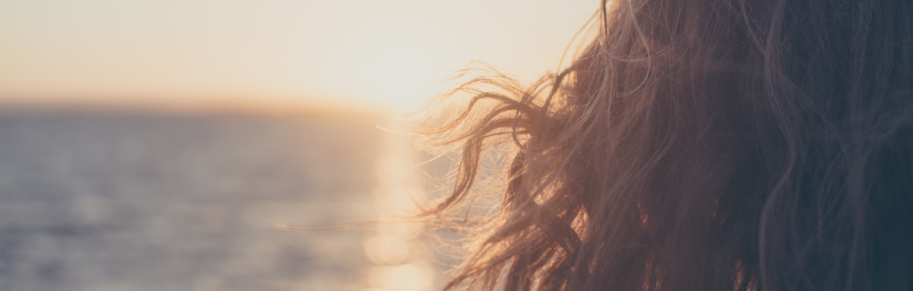 Woman with long hair zoomed in with sunset at the beach background