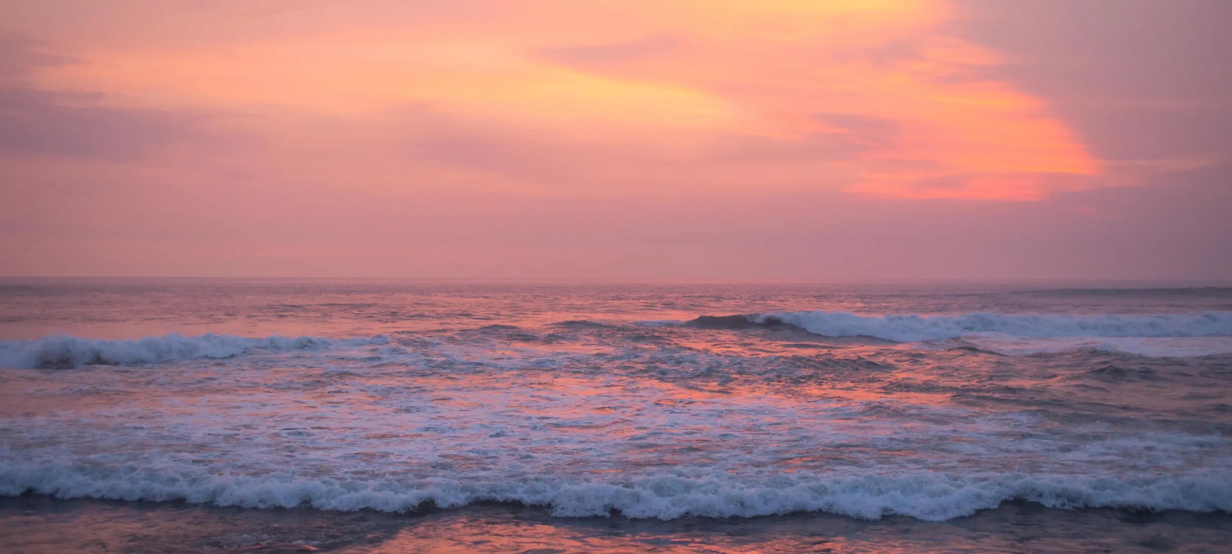 Sunset over the ocean with pink and orange hues in the sky.
