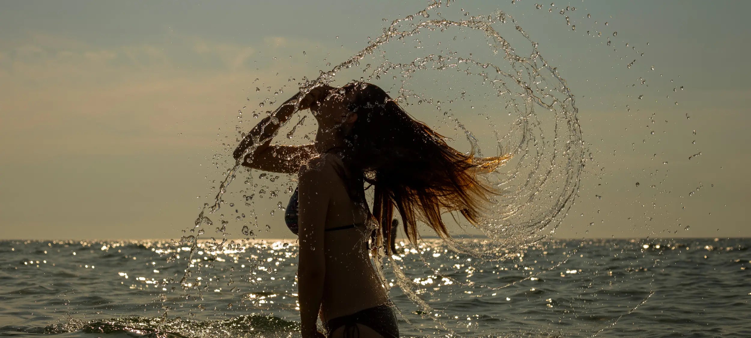 Person playing in the water with a splash, sunset over the ocean